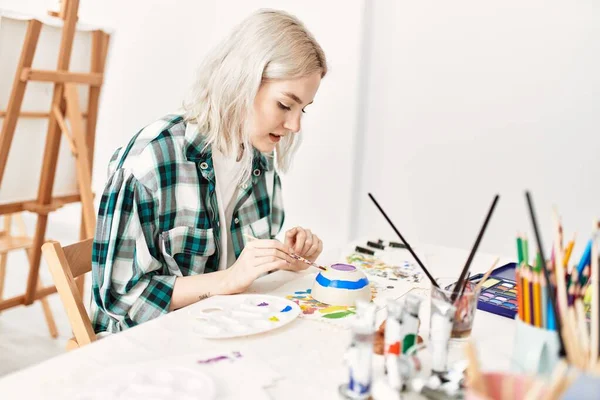 Genç sanatçı kız resim atölyesinde rahatça çömlek boyuyor..