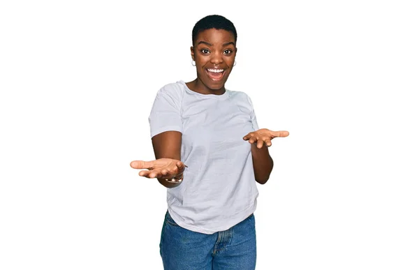 年轻的非洲裔美国女人穿着休闲的白色T恤 笑容满面 张开双臂表示友好的欢迎 积极而自信的问候 — 图库照片