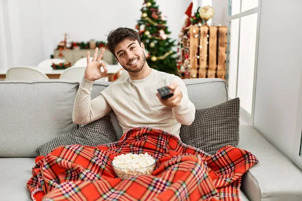 Ung Latinamerikansk Man Äter Popcorn Sitter Soffan Julgran Gör Tecken — Stockfoto