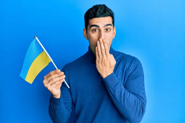 Bonito Hispânico Vestindo Bandeira Ucraniana Cobrindo Boca Com Mão Chocado — Fotografia de Stock
