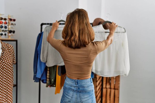 Young caucasian customer woman on back view choosing clothes at clothing store.