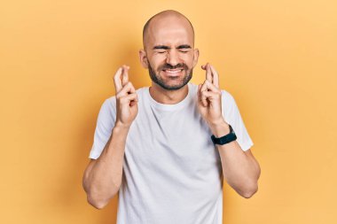 Genç kel bir adam, günlük beyaz tişörtler giyip umut ve gözlerin kapalı bir şekilde parmaklarını çaprazlayarak işaret ediyor. Şans ve batıl inançlar. 