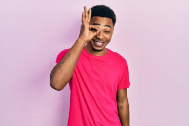 Casua tişörtü giyen genç Afro-Amerikan bir adam el hareketleriyle gülümsüyor ve mutlu yüzüyle parmaklarının arasından bakıyor.. 
