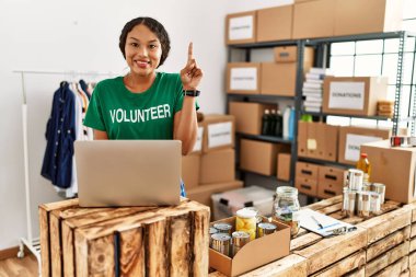 Güzel İspanyol kadın gönüllü tişört giyiyor. Bilgisayarla çalışıyor. Bir fikir ya da soruyla şaşırmış. 