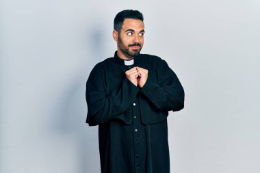 Sakallı yakışıklı, Katolik rahip cübbesi giyen, elleri çenesinde gergin ve heyecanlı bir şekilde yan tarafa bakan bir İspanyol. 