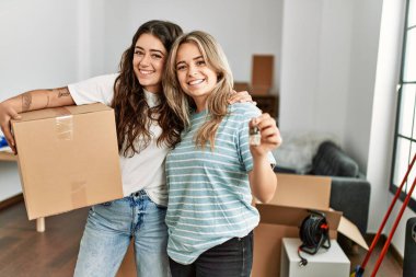 Mutlu bir şekilde gülümseyen genç çift yeni evin anahtarını ve karton kutuyu tutuyor..