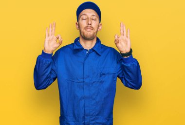 Sakallı, inşaatçı tulumu giyen kel adam rahatlamış ve parmaklarıyla meditasyon hareketi yaparken gözleri kapalı gülümsüyor. yoga konsepti. 