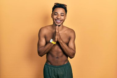 Afro-Amerikan genç adam mayo ve yüzücü gözlüğü takıyor ellerimle dua edip af diliyor kendinden emin bir şekilde gülümsüyor.. 