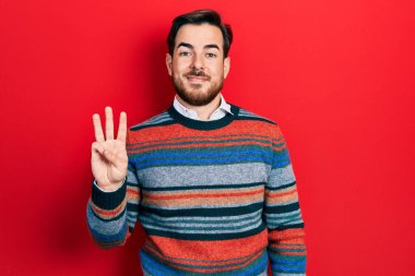 Sakallı, zarif yün kazak giyen yakışıklı beyaz adam üç numarayı gösterip gülümseyerek kendinden emin ve mutlu görünüyor.. 