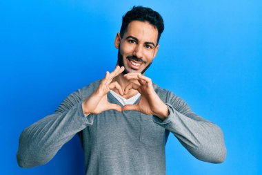 Gündelik beyaz tişört giyen, aşık gülümseyen, elleriyle kalp sembolü yapan genç İspanyol adam. romantik kavram. 