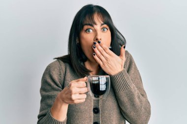 Genç İspanyol kadın bir fincan kahve içiyor. Ağzını eliyle kapatıyor. Şok geçiriyor ve hata yapmaktan korkuyor. şaşırmış ifade 