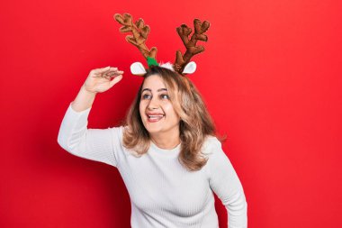 Orta yaşlı beyaz kadın şirin Noel geyiği boynuzları takıyor çok mutlu ve gülümsüyor başlarını kaldırarak uzaklara bakıyor. arama kavramı. 