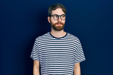 Kafkasyalı sakallı, çizgili tişört ve gözlüklü, gülümseyen ve kafasını çeviren bir adam.. 