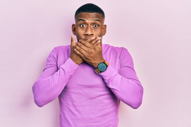 Gündelik pembe kazak giyen genç siyah adam yanlışlıkla elleri ile ağzını kapatırken şok oldu. gizli kavram. 