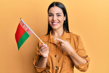 Beyaz bayrak tutan genç esmer kadın mutlu bir şekilde el ve parmak işareti yapıyor. 