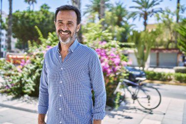 Orta yaşlı İspanyol gülen adam şehirde mutlu bir şekilde duruyor..