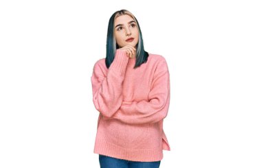 Pembe yün kazak giyen, elleri çenesinde soru soran, düşünceli bir genç modern kız. Düşünceli bir yüzle gülümsüyor. şüphe kavramı. 