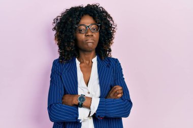 Genç Afro-Amerikan kadın iş kıyafetleri ve gözlük takıyor şüpheci ve gergin, yüzünde çapraz kollarla onaylamayan bir ifade var. negatif kişi. 