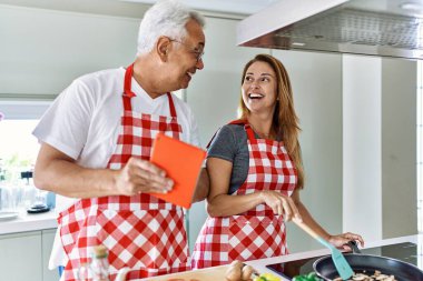 Orta yaşlı İspanyol çift gülümsüyor. Mutfakta yemek pişiriyor ve dokunmatik ped kullanıyor..