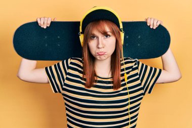 Kulaklık takmış, kaykay tutan kızıl saçlı genç bir kadın. Depresyonda ve endişe içinde. Kızgın ve korkmuş bir şekilde ağlıyor. hüzünlü ifade. 