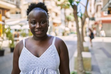 Genç Afrikalı Amerikalı kadın gülümseyerek şehirde mutlu mesut duruyor..