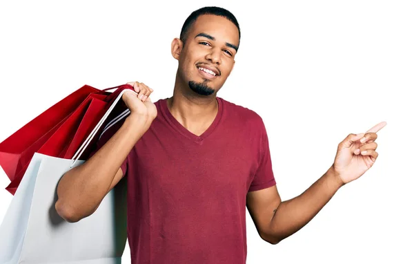 Joven Hombre Afroamericano Sosteniendo Bolsas Compras Sonriendo Feliz Señalando Con —  Fotos de Stock