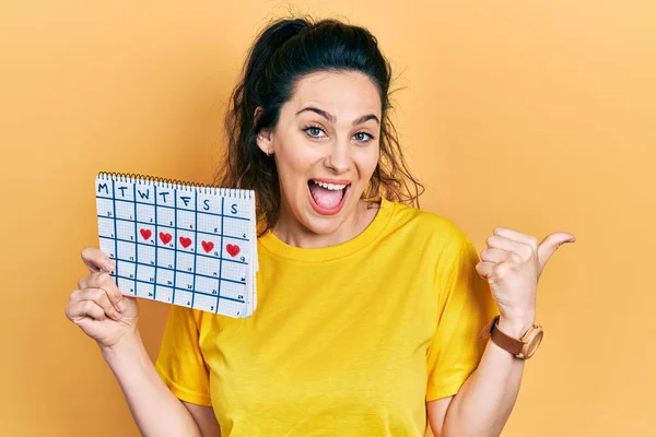 Joven Mujer Hispana Sosteniendo Calendario Del Corazón Apuntando Con Pulgar — Foto de Stock