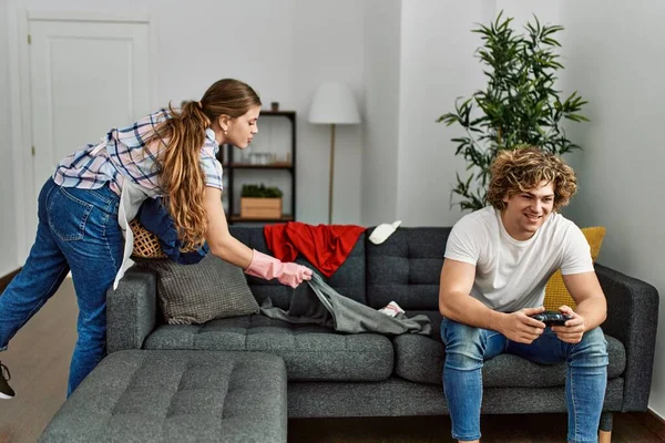 Woman doing laundry while man plays video game at home.