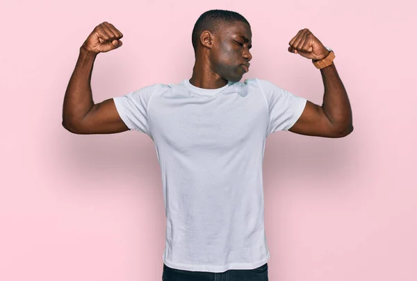 腕の筋肉が誇らしげに笑っているのを示すカジュアルな白いTシャツを着た若いアフリカ系アメリカ人男性 フィットネスのコンセプト — ストック写真