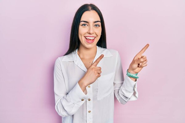 Beautiful woman with blue eyes wearing casual white shirt smiling and looking at the camera pointing with two hands and fingers to the side. 