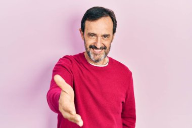 Orta yaşlı İspanyol bir adam günlük giysiler içinde gülümseyerek dostça el sıkışarak selamlama ve hoş geldin diyor. başarılı iş. 