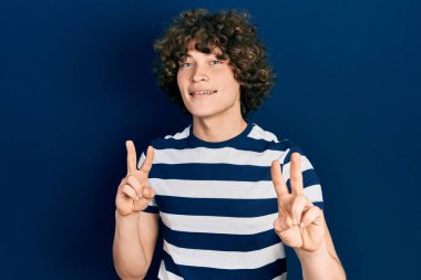 Sıradan çizgili tişört giyen yakışıklı genç adam kameraya bakıp zafer işareti yapıyor. İki numara.. 