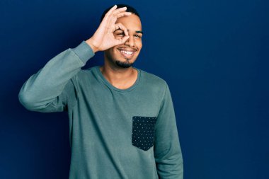 Genç Afro-Amerikan adam günlük kıyafetler giyiyor gülümsüyor mutlu bir şekilde el pençe divan duruyor. 