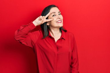 Orta yaşlı İspanyol kadın gündelik kıyafetler giyip barış sembolü yapıyor. Yüzünde parmakları, gülümseyerek zaferini gösteriyor. 