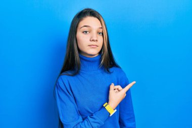 Balıkçı yaka kazak giyen genç esmer kız, el parmağı yanda, ciddi ve sakin bir yüz ifadesi sergiliyor. 