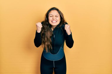 Kolları havada ve gözleri kapalı zaferi kutlayan dalgıç neoprene üniforması giyen genç İspanyol kız. Kazanan konsept. 