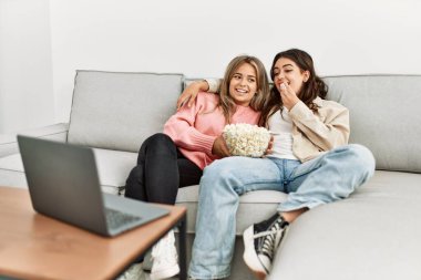 Genç çift film izliyor ve patlamış mısır yiyor. Evdeki koltukta oturuyorlar..