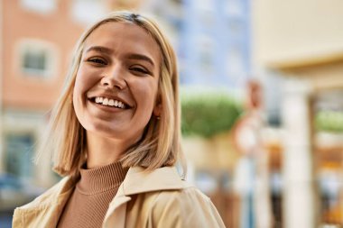 Genç sarışın kız gülümsüyor, mutlu bir şekilde şehirde duruyor..