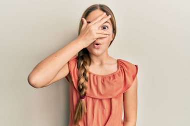 Güzel, esmer, yaz tişörtü giyen küçük bir kız. Şoka girmiş, yüzünü ve gözlerini kapamış, parmaklarından korkuyla bakıyor. 