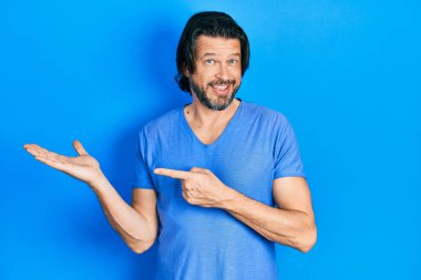 Orta yaşlı, günlük kıyafetler giyen beyaz bir adam kameraya hayret ediyor ve gülümsüyor.. 