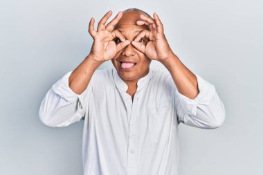 Orta yaşlı Latin bir adam sıradan kıyafetler giyiyor dürbün gibi jest yapıyor, gözleri parmaklarından bakıyor. çılgın ifade. 