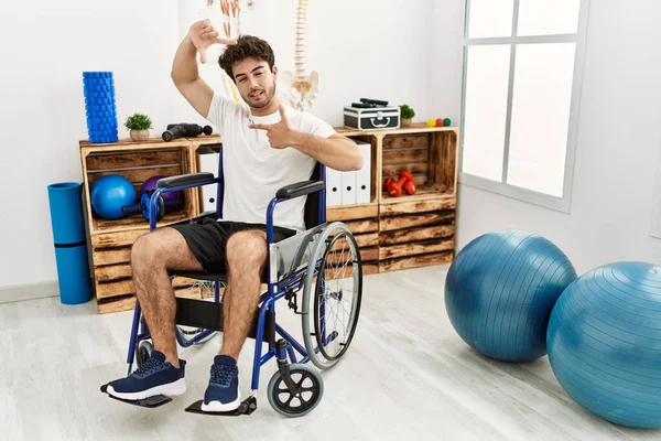 Hombre Hispano Sentado Silla Ruedas Clínica Fisioterapia Sonriendo Haciendo Marco —  Fotos de Stock