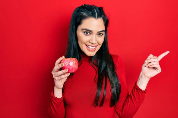 Mladý Hispánec Dívka Drží Červené Jablko Úsměvem Šťastný Ukazuje Rukou — Stock fotografie