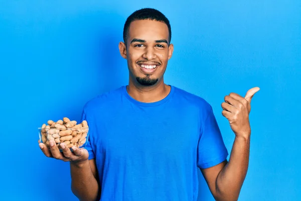 Joven Afroamericano Hombre Sosteniendo Tazón Cacahuetes Señalando Pulgar Hacia Lado — Foto de Stock