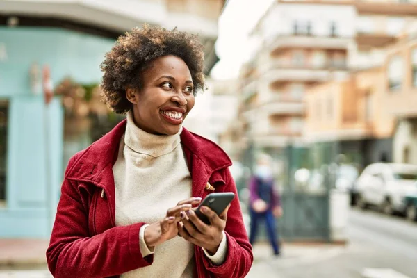 アフロの髪を持つ美しいビジネスアフリカ系アメリカ人女性は スマートフォンを使用して街で幸せと自信を持って屋外で笑顔 — ストック写真