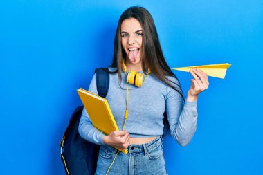 Elinde kitap ve kağıt uçak tutan genç esmer öğrenci komik bir ifadeyle dilini dışarı çıkartıyor.. 