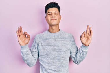 Günlük kıyafetler giyen genç İspanyol adam rahatla ve gözleri kapalı gülümse parmaklarıyla meditasyon hareketi yapıyor. yoga konsepti. 