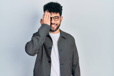 Sakallı genç Arap adam bir gözünü eliyle kapatıyor, yüzünde kendine güvenen bir gülümseme ve şaşırtıcı bir duygu var.. 