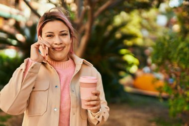 Genç İspanyol kız akıllı telefondan konuşuyor ve şehirde kahve içiyor..