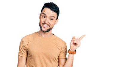 Sakallı, sıradan tişörtlü, yüzünde kocaman bir gülümseme olan İspanyol bir adam. Elinle kameraya bakıyor.. 